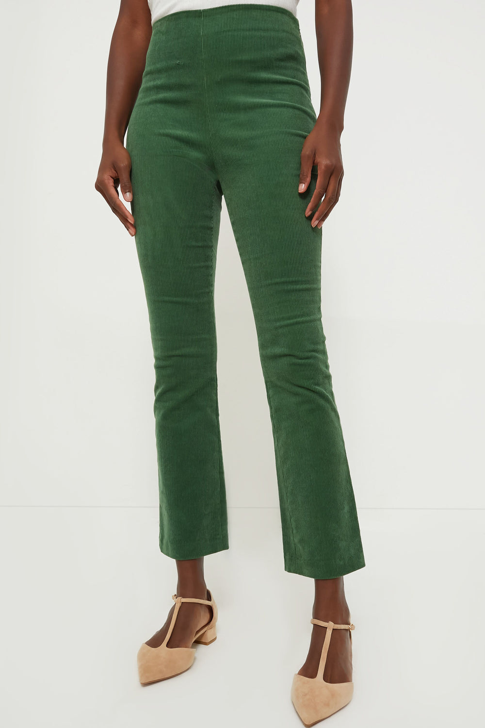 A person stands in high-waisted Tuckernuck green corduroy pants with a cropped kick hem, paired with beige pointed-toe shoes.