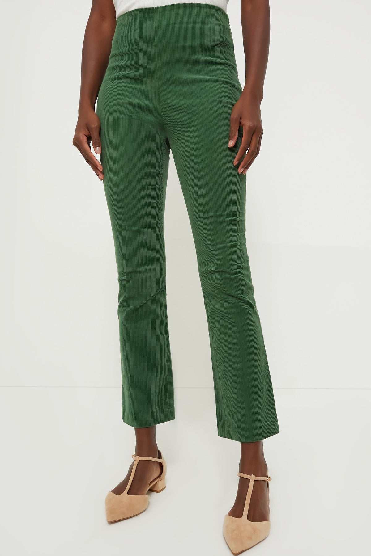A person stands in high-waisted Tuckernuck green corduroy pants with a cropped kick hem, paired with beige pointed-toe shoes.