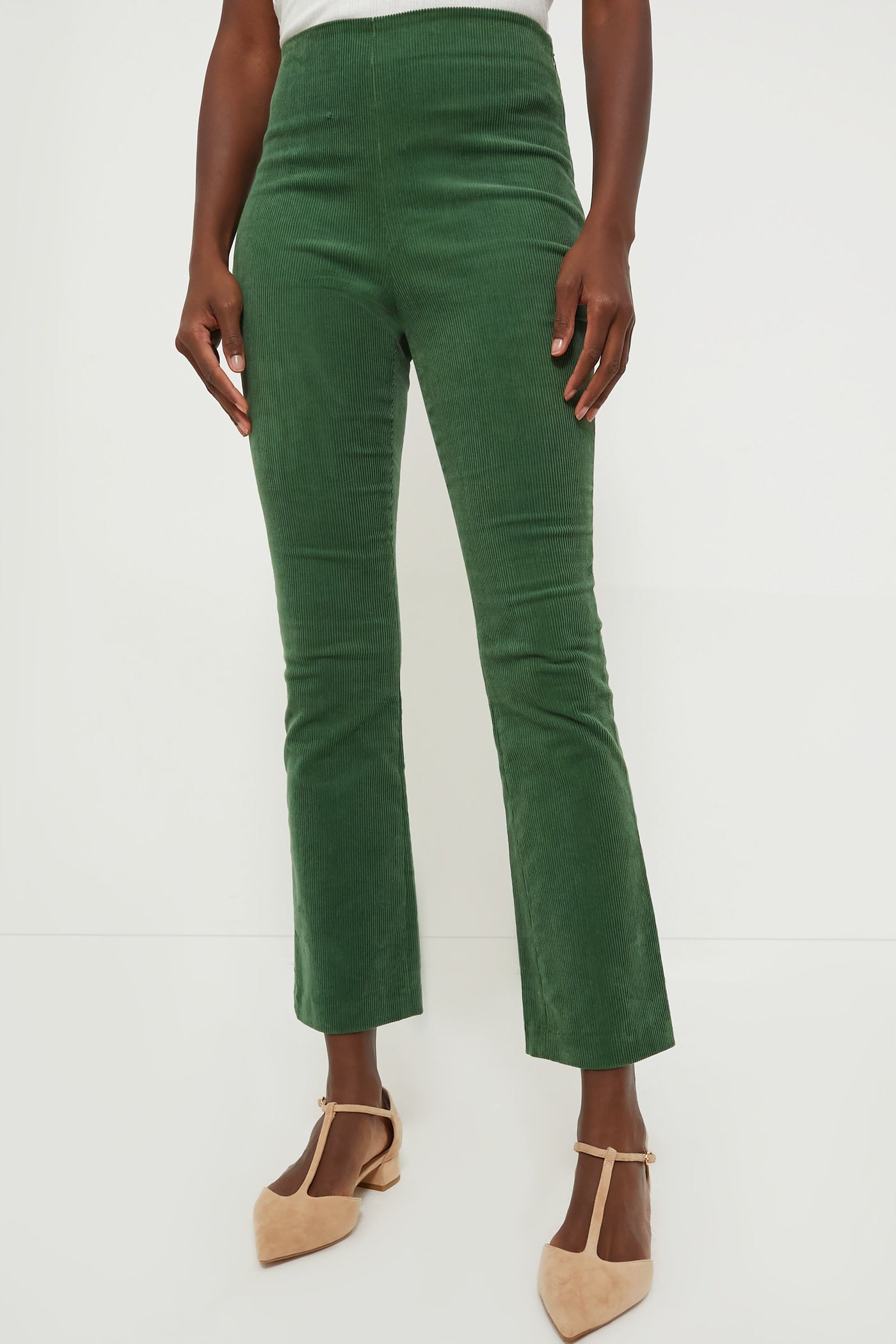A person stands in high-waisted Tuckernuck green corduroy pants with a cropped kick hem, paired with beige pointed-toe shoes.