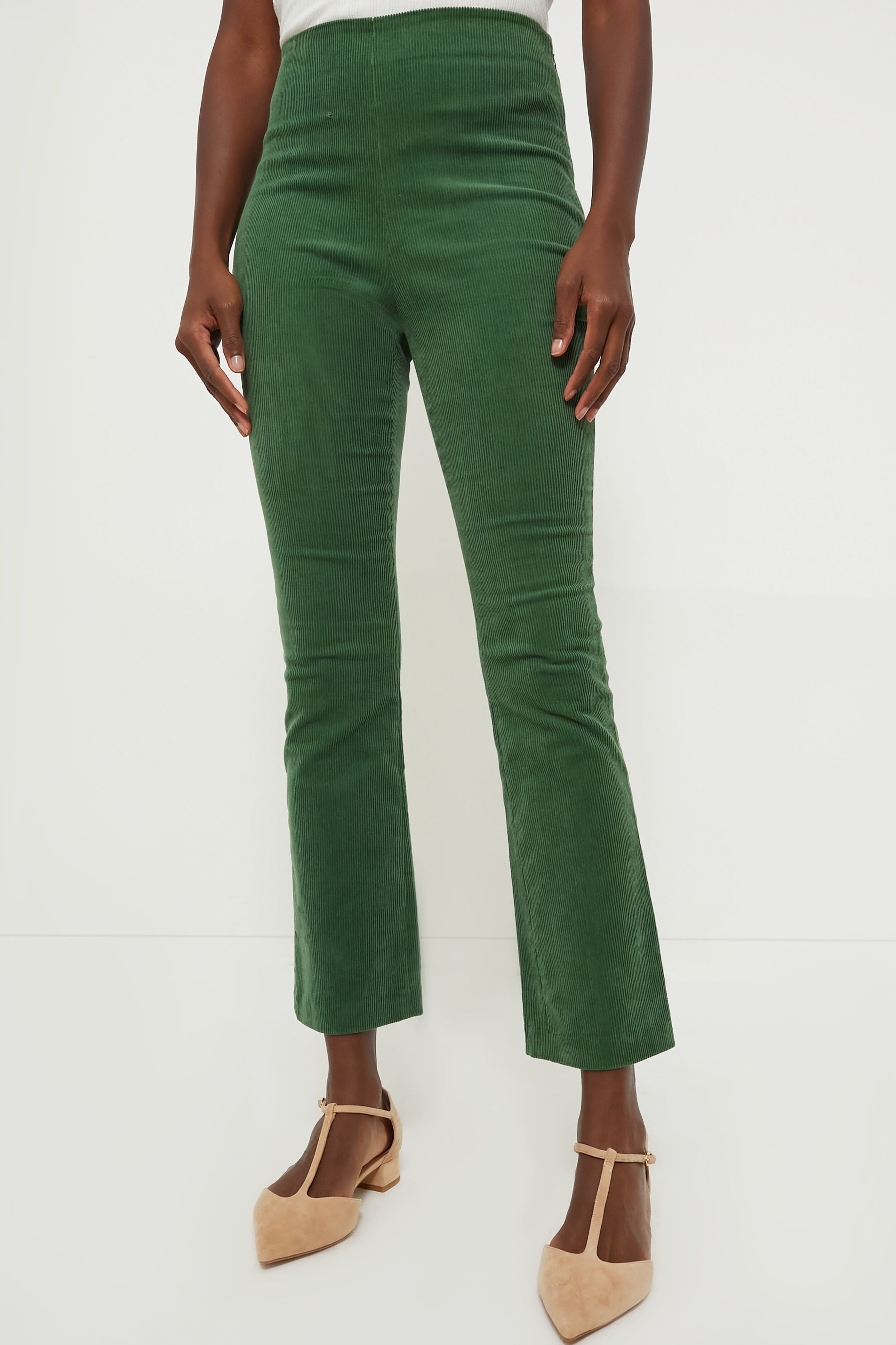 A person stands in high-waisted Tuckernuck green corduroy pants with a cropped kick hem, paired with beige pointed-toe shoes.