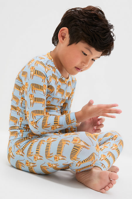 Child in classic Tigers Kids Bamboo Pj Set, effortlessly examining fingers. Light blue, breathable bamboo fabric, perfect for fun, cozy moments. High-end comfort meets playful design.