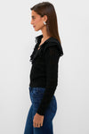 Young woman models the Black Pointelle Knit Sherry Top, featuring a ruffled lace V-neckline and pointelle knit, paired with dark jeans for an effortless, classic look.
