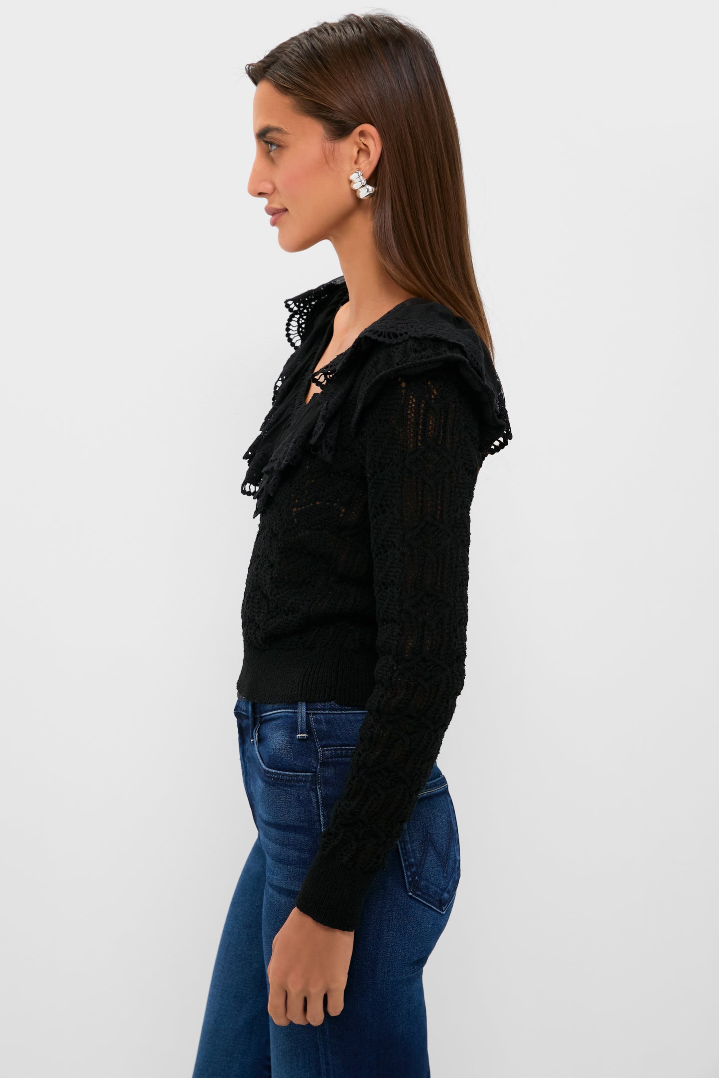 Young woman models the Black Pointelle Knit Sherry Top, featuring a ruffled lace V-neckline and pointelle knit, paired with dark jeans for an effortless, classic look.