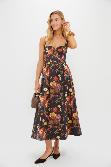 A woman wears a Tuckernuck Baroque Floral fit-and-flare midi dress with a sweetheart neckline, styled with a brown handbag, black heels, and gold bangles, posed against a plain white background.