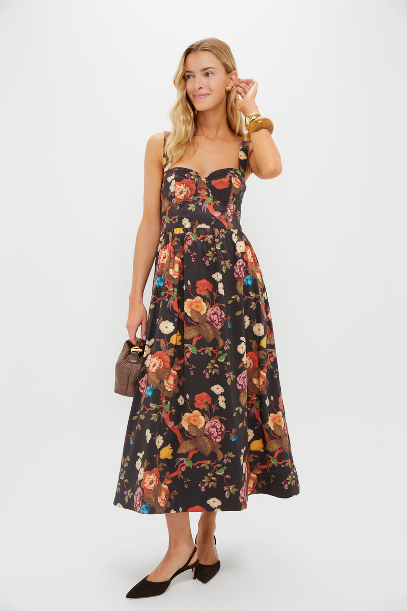 A woman wears a Tuckernuck Baroque Floral fit-and-flare midi dress with a sweetheart neckline, styled with a brown handbag, black heels, and gold bangles, posed against a plain white background.