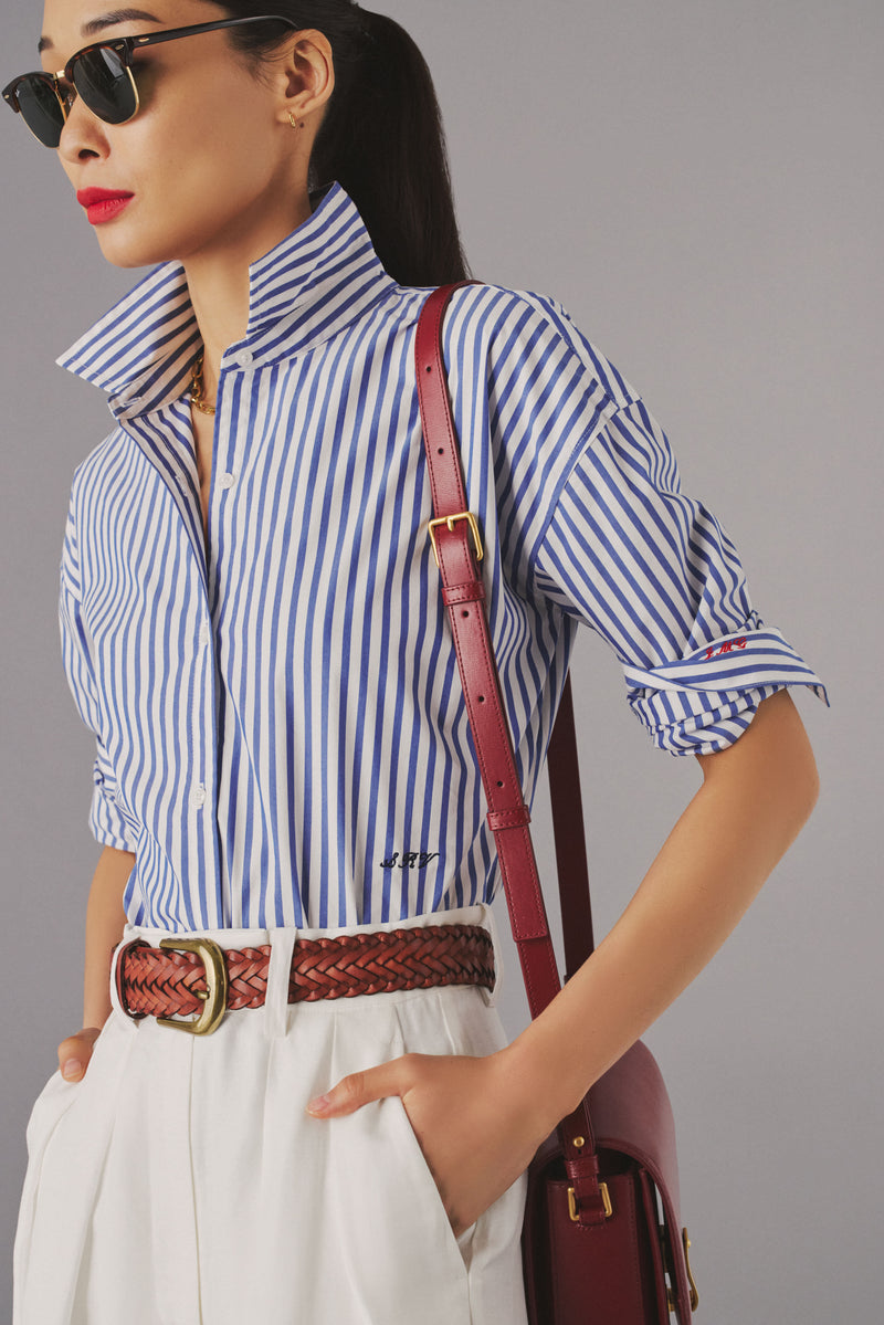 Woman in sunglasses and a blue and white striped shirt with initials monogrammed onto the waist. 
