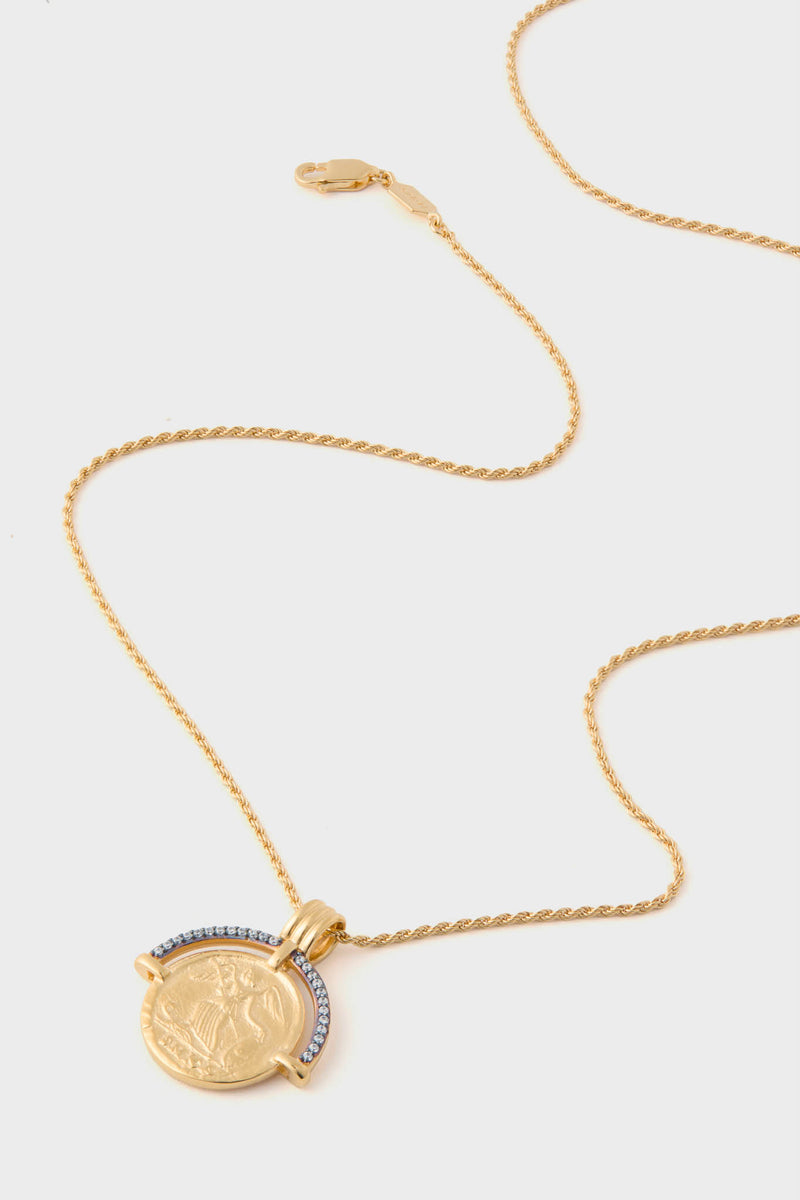 Missoma gold chain necklace with a round, coin-like pendant showcasing an embossed design and a row of clear stones along part of the edge.