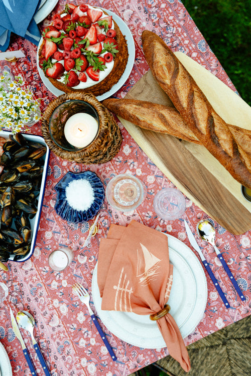 A summer table with a cake covered in strawberries, mussels, and two baguettes. 