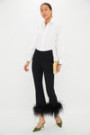 A person in a white button-up shirt, Tuckernuck Black Feather Knit Ashford Pants with feather-trimmed hem, green heels, and a beige clutch stands against a plain white background—these pants are perfect for making a statement at any party.