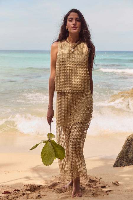 Woman on a beach in a classic, effortless gold metallic star lace Keating top, embodying a high-end, relaxed vibe, perfect for fun and stylish occasions.