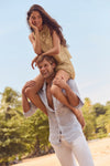 Young man on a beach carrying a woman, showcasing the high-end, classic Summer Classic Stripe Laguna Linen Shirt—effortless and fun, perfect for any warm weather adventure.