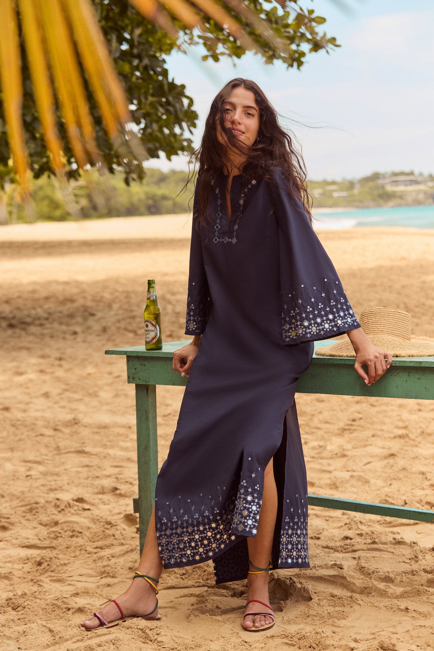 Young woman in a classic navy dress showcases Rainbow Constantia Sandals, featuring multi-colored straps and a wrap-around ankle strap, embodying effortless, high-end summer style.
