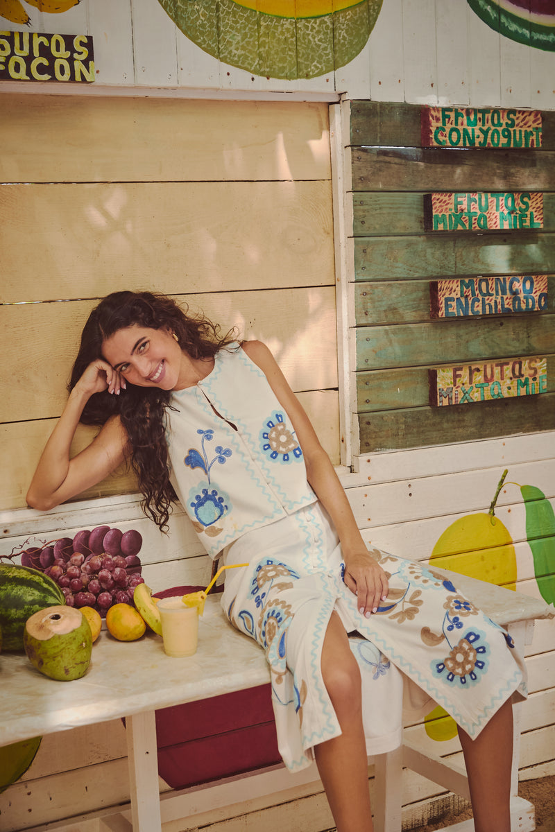 Folk Flower Embroidered Luna Top: A classic, effortlessly chic embroidered top, perfect for a fun, high-end summer look, shown in a vibrant fruit stand setting.