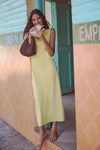 Young woman in a Lemongrass Kingston Knit Dress, exuding effortless charm, holds an empanada at a juice shop, embodying Tuckernuck's classic and fun style.
