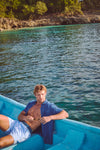 Young man in a boat wearing a classic Indigo Basketweave Short Sleeve Palma Linen Shirt, enjoying an effortless, fun day out; embodies high-end, relaxed style.