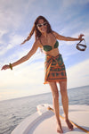 Woman on a boat wearing the Rust and Dark Green Dance of Pareo, a classic and effortless wrap-skirt, holding a snorkel mask, enjoying a fun, high-end ocean adventure.