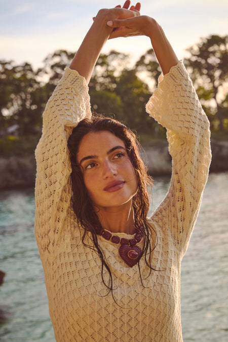 Young woman at shore wearing the Burgundy Lira Necklace, featuring a bold heart pendant with red carnelian, embodying a classic, effortless, high-end style.