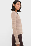 A woman wears a beige, textured, long-sleeve knit cardigan with ruffle-trimmed cuffs, styled with a brown skirt.