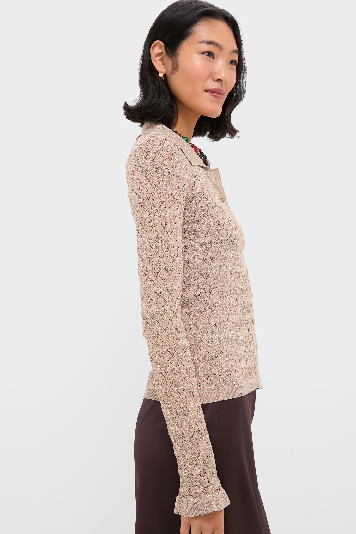 A woman wears a beige, textured, long-sleeve knit cardigan with ruffle-trimmed cuffs, styled with a brown skirt.
