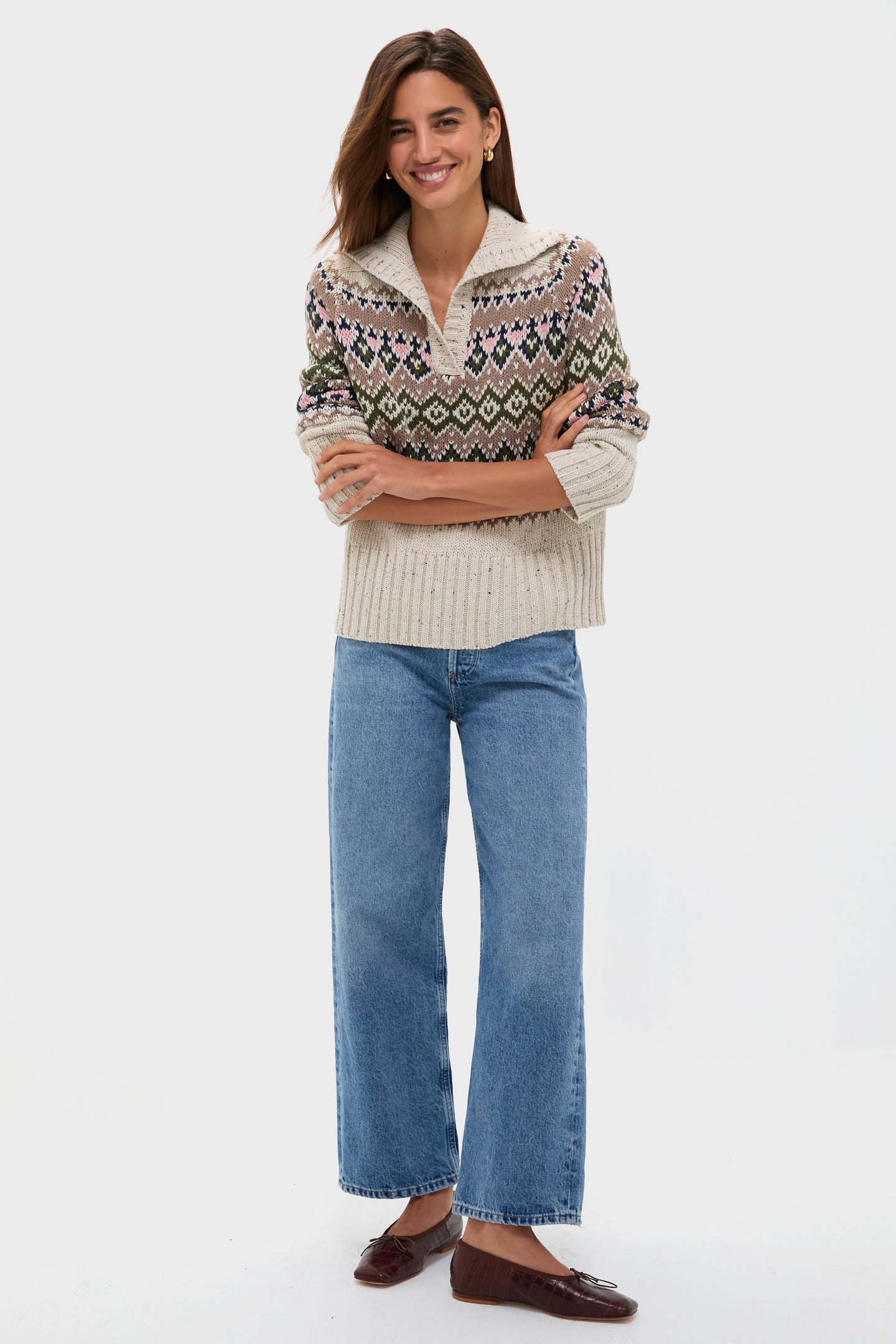 A woman smiles in a Hyacinth House relaxed fit sweater, wide-leg blue jeans, and brown flats against a plain white background.