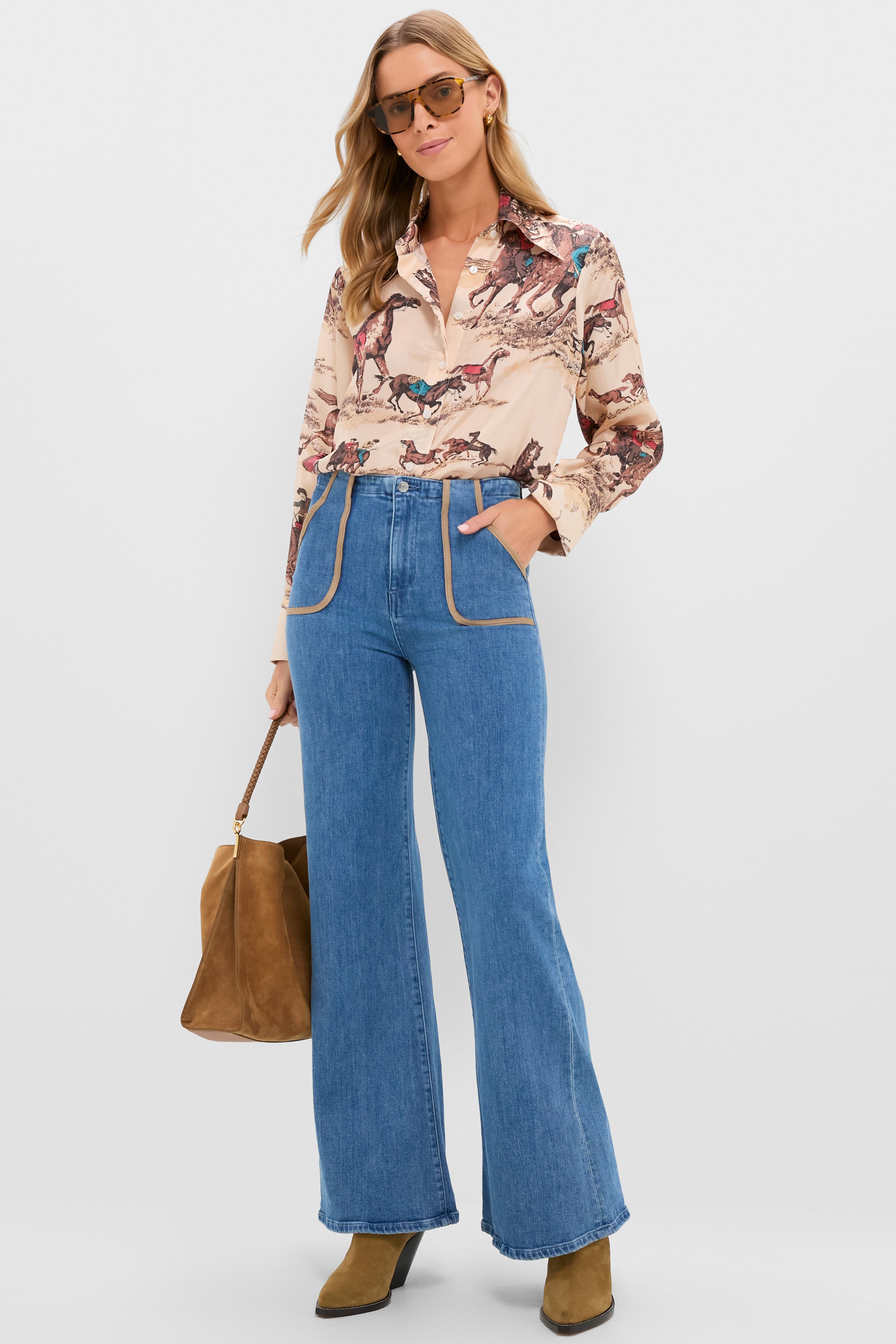 A woman wears an Alix of Bohemia horse print shirt with high-waisted flared jeans, tan boots, sunglasses, and carries a brown suede handbag.