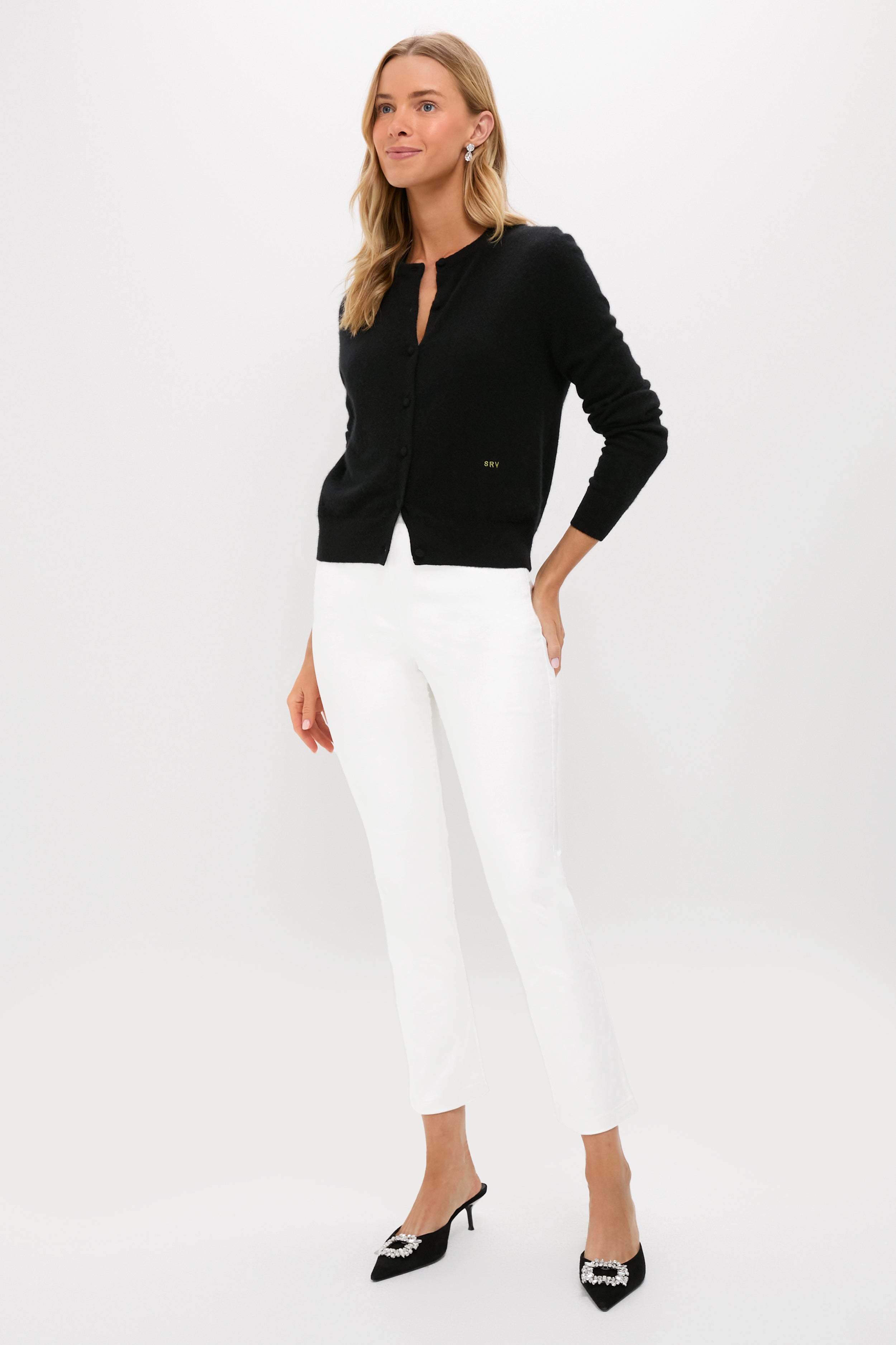 Model showcases classic Winter White Velvet Ashford Pants with a black cardigan, achieving an effortless, high-end look, complemented by black mule heels with jeweled buckles.