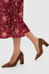 A person wearing a red floral skirt and brown Schutz suede pumps stands on a light background.