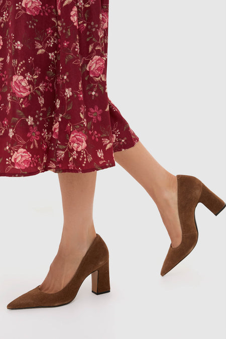 A person wearing a red floral skirt and brown Schutz suede pumps stands on a light background.