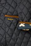 Close-up of a black Barbour x Tuckernuck jacket featuring diamond quilting, brown corduroy trim on the pocket and cuff, and floral lining visible at the cuff.