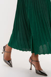 Model showcasing the Green Shimmer Knit Cammie Maxi Dress, highlighting its classic, metallic-sheen pleats, paired with effortless, fun gunmetal slingback pumps, evoking a high-end style.