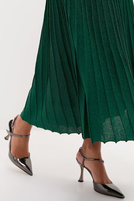Model showcasing the Green Shimmer Knit Cammie Maxi Dress, highlighting its classic, metallic-sheen pleats, paired with effortless, fun gunmetal slingback pumps, evoking a high-end style.