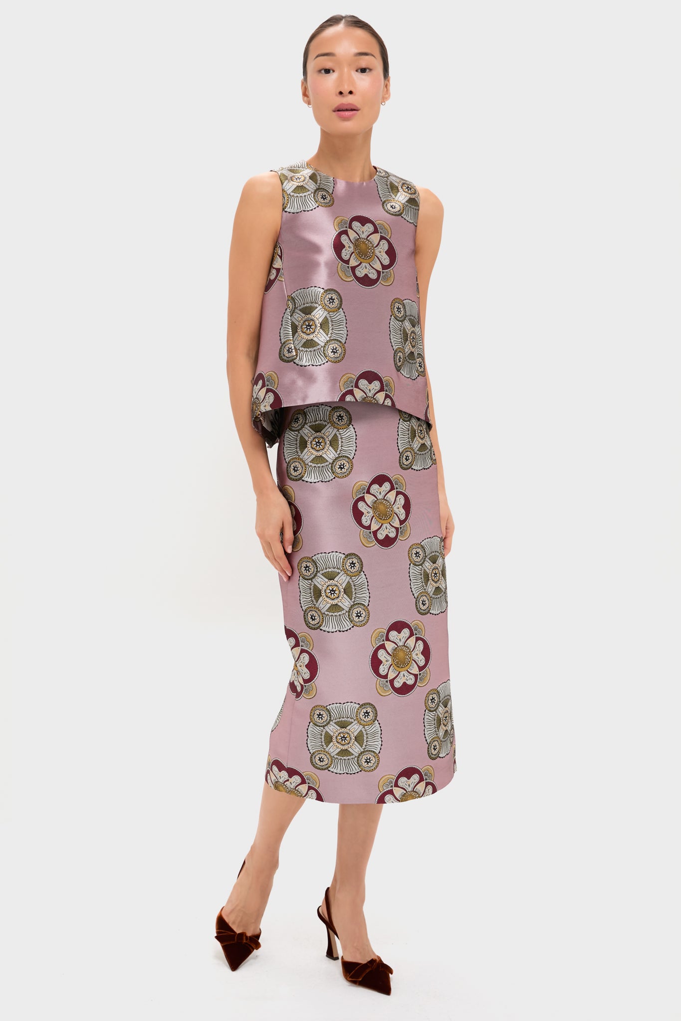 A woman wears a sleeveless pink La DoubleJ top with a matching nucleus-print silk jacquard midi skirt featuring owl and floral motifs, paired with brown heels.