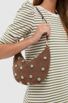 Woman wearing a striped top holds the classic, high-end Choco Bar Smooth Nubuck with Studs Lune Bag, featuring effortless silver studs and a fun, knotted strap.