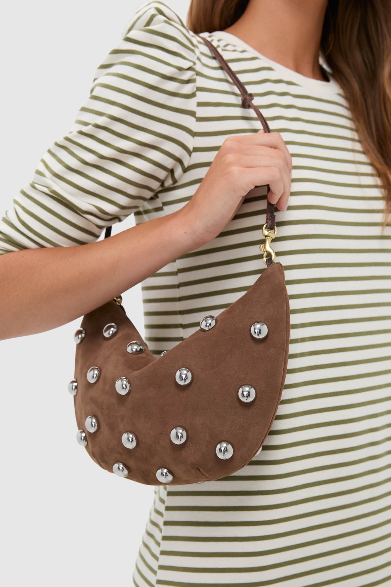 Woman wearing a striped top holds the classic, high-end Choco Bar Smooth Nubuck with Studs Lune Bag, featuring effortless silver studs and a fun, knotted strap.