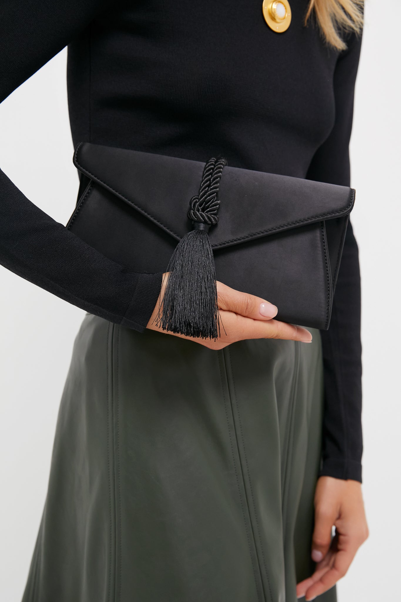 Woman holding the classic Black Satin Gabrielle Clutch with braided tassel, showcasing its effortless, high-end design perfect for fun, sophisticated occasions.