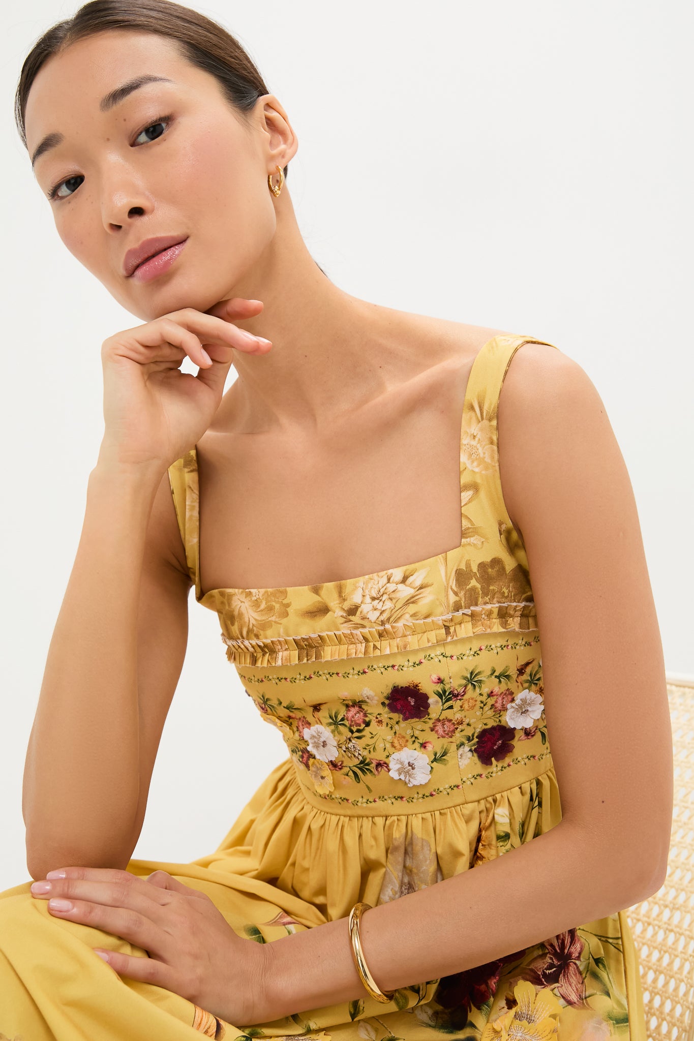 Paramo Barbara Maxi Dress: A young woman models this classic, high-end sundress with effortless style, featuring a floral print and pleated trim, accessorized with gold jewelry.