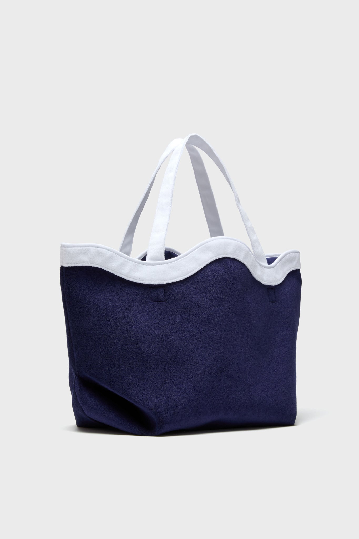 A Tuckernuck Accessories navy blue terrycloth tote bag with wavy white trim and two white handles, perfect for carrying beach essentials, shown against a plain light background.
