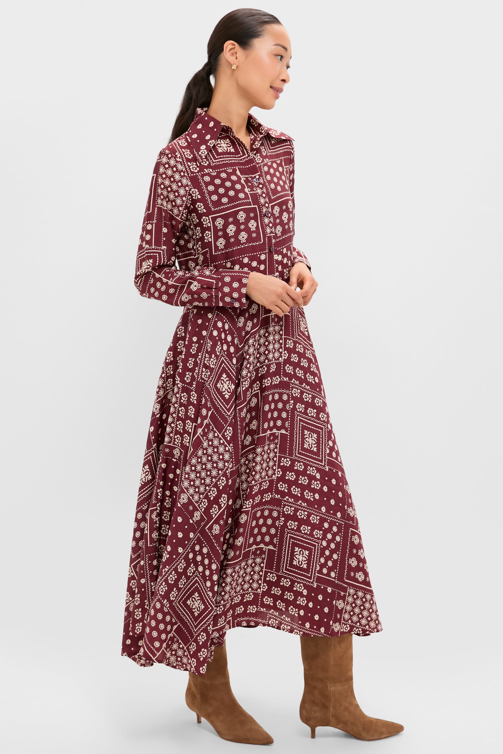 A woman wears an Alix of Bohemia vintage-inspired panel dress with long sleeves, a burgundy pattern, a collar, and brown knee-high boots, standing against a plain light background.