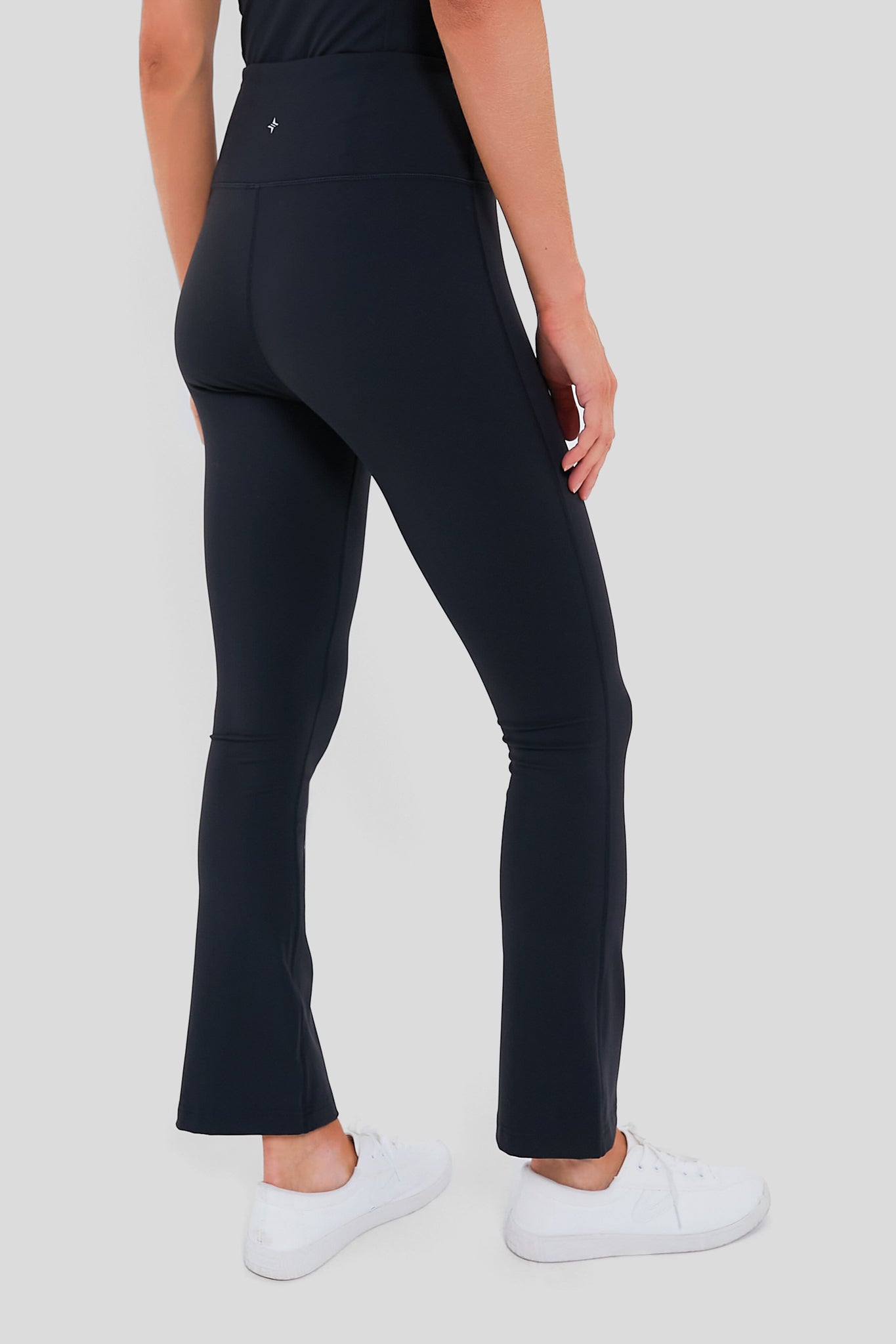 Classic Black High Rise Compression Spandex Millie Yoga Pants, showcasing an effortless, flattering fit with slightly flared bottoms, paired with simple white athletic sneakers.