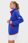 Woman in a classic Blue and Red Fleece Cady Quarter Zip pullover with contrasting trim, highlighting its effortless, high-end design. She pairs it with a white skirt.