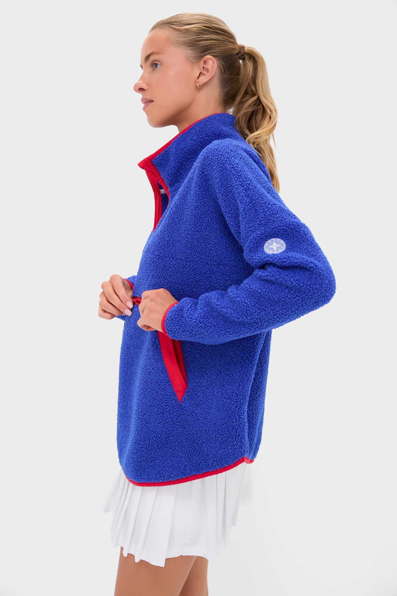 Woman in a classic Blue and Red Fleece Cady Quarter Zip pullover with contrasting trim, highlighting its effortless, high-end design. She pairs it with a white skirt.