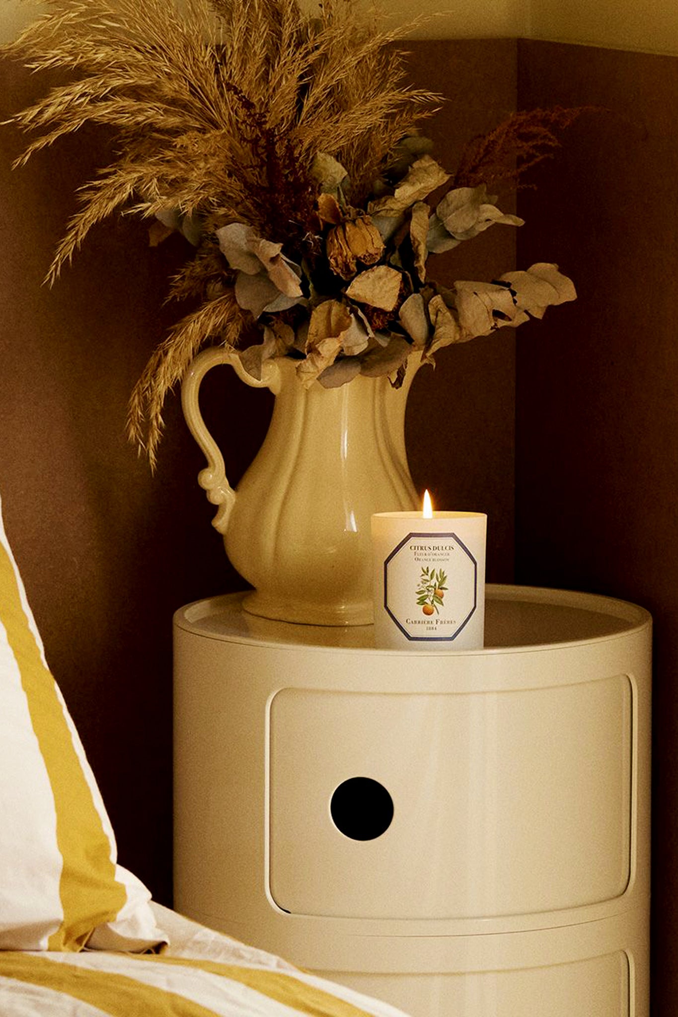 Blossom Candle by Carrière Frères, elegantly displayed on a classic cream bedside cabinet, exudes an effortless, high-end ambiance with its sweet, floral fragrance and botanical artwork.