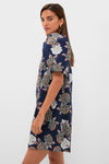 Young woman models the Navy Floral Mimi Mini Dress featuring puff sleeves and a ruffle collar, exuding classic, effortless style with a fun, high-end floral pattern.