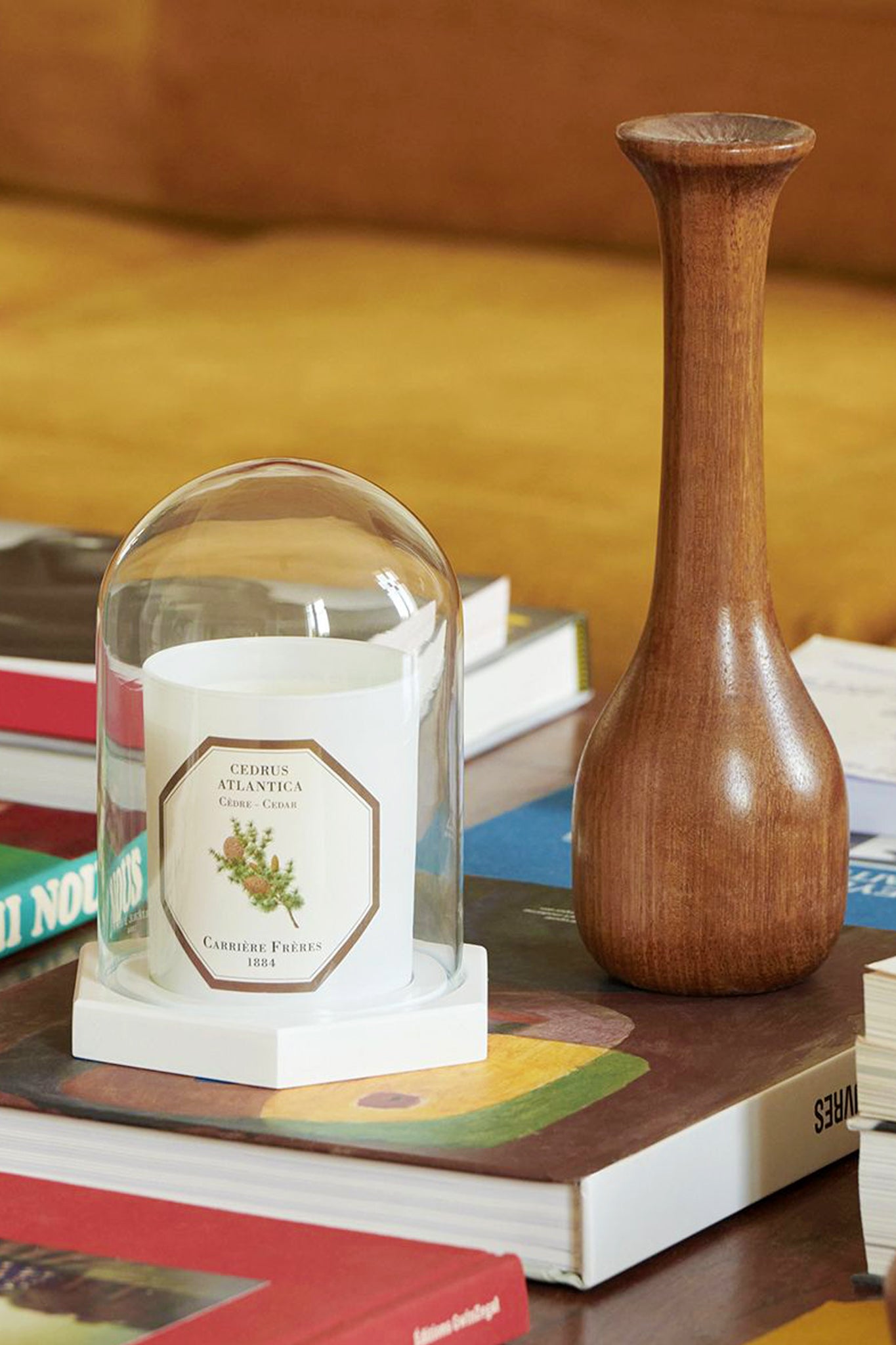 Cedar Candle by Carrière Frères under glass cloche on art books. Classic and effortless, this high-end fragrance brings fun, woody notes perfect for gifting.