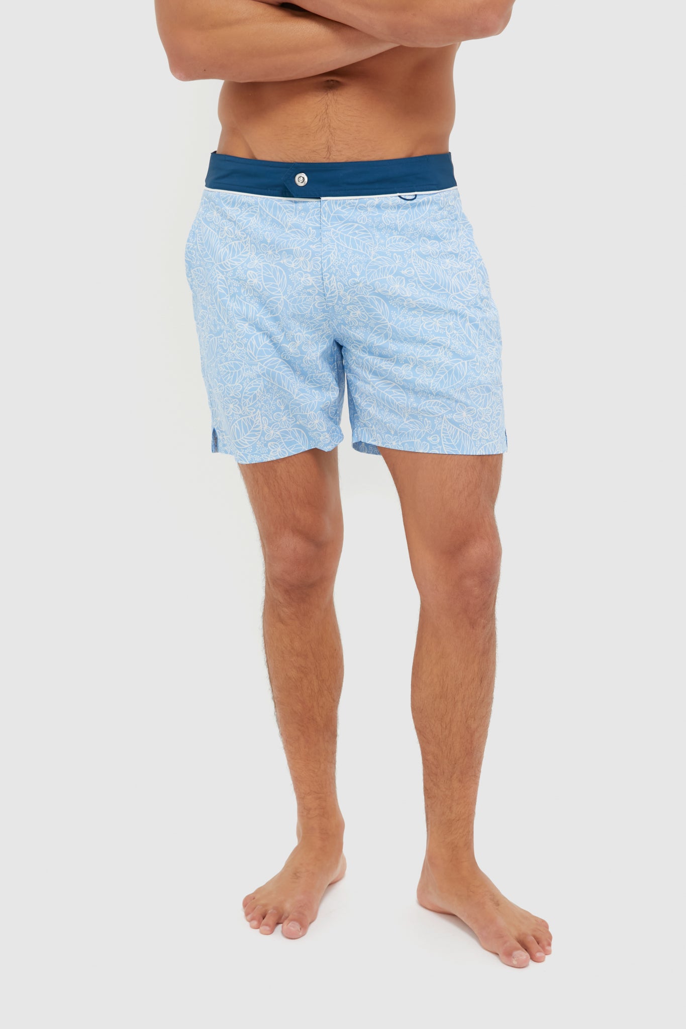 A man stands barefoot with arms crossed, wearing Spruce light blue patterned quick-dry swim shorts featuring a dark blue waistband.