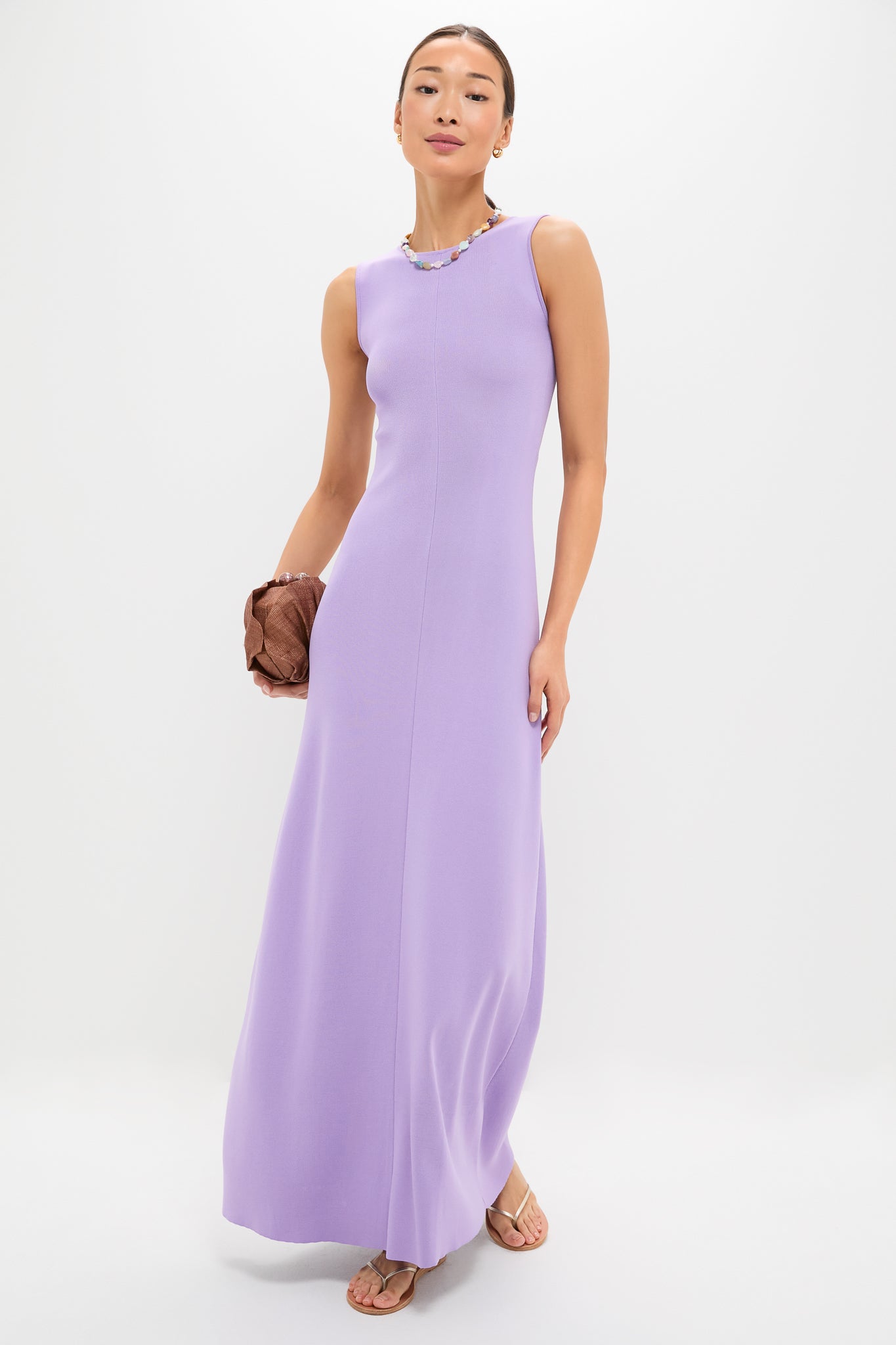 Model in a sleeveless lavender maxi dress, holding a Cocoa Origami Scallop Clutch. The look is classic and effortless, enhanced by a fun, multicolored necklace.