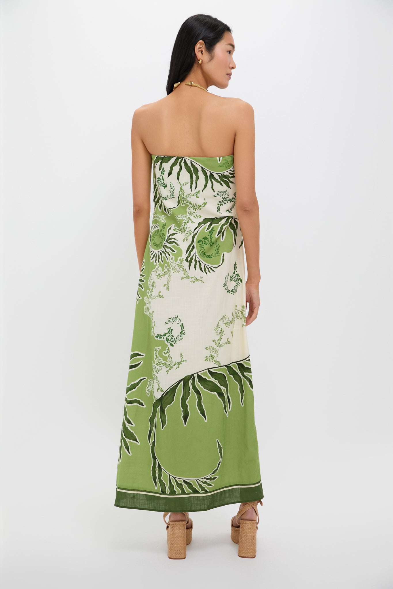 Back view of a person in the Ireland Green Wess Midi Dress, featuring a classic strapless design with bold leaf motifs and a sleek side slit.