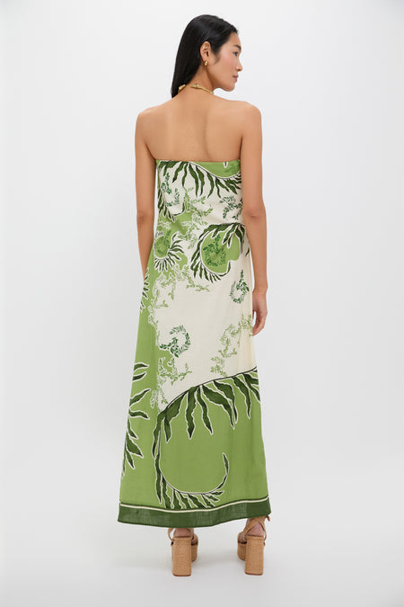Back view of a person in the Ireland Green Wess Midi Dress, featuring a classic strapless design with bold leaf motifs and a sleek side slit.