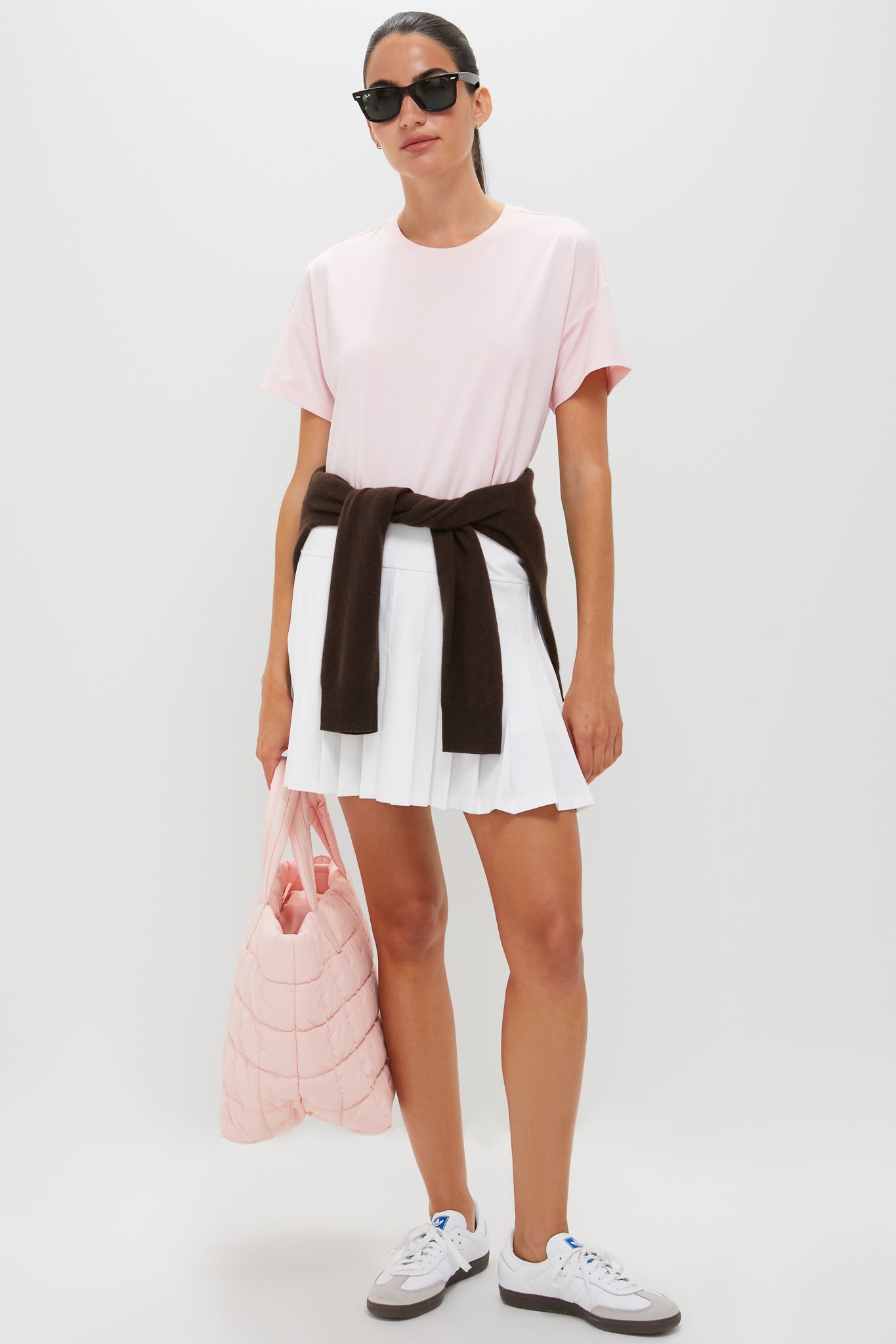 Woman in a classic, effortless light pink Ryan Boyfriend Tee and white mini skirt, paired with sneakers, sunglasses, and a quilted tote, exuding high-end, fun style.