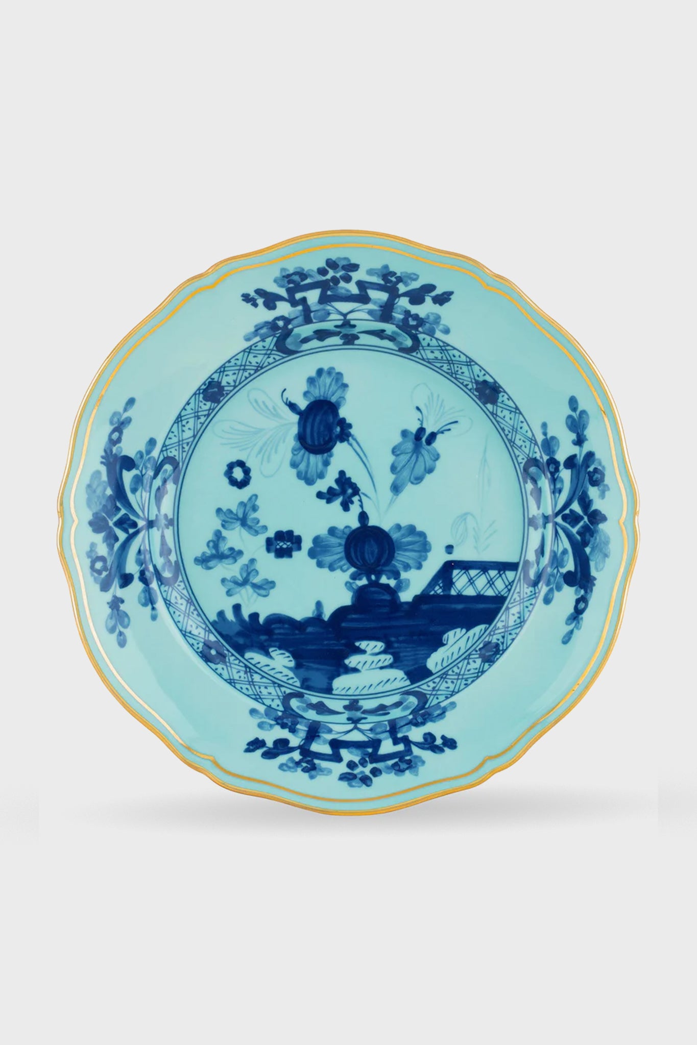 The Ginori 1735 Oriente Italiano Iris dinner plate showcases scalloped Ginori porcelain, gold trim, and blue floral and bridge motifs, exemplifying handcrafted Italian artistry.